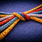 Meerdere kleurrijke touwen die vanuit een centrale verbinding uit elkaar lopen als metafoor voor samenwerking zonder uniformiteit