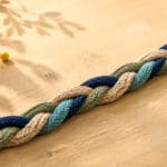 Een gevlochten streng van gekleurde touwen ligt op een houten tafel met een kleine gele bal.